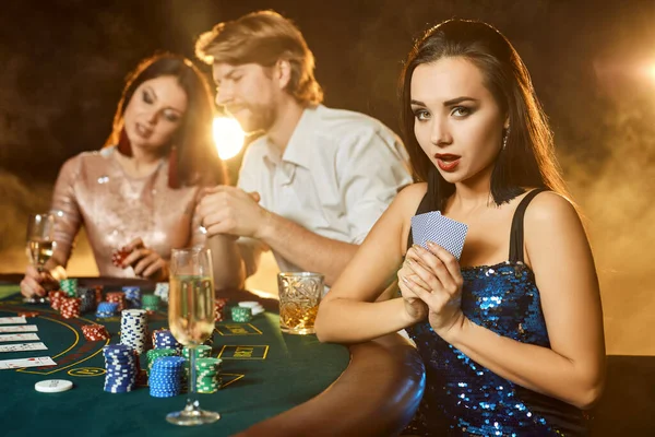 Group of an elegant people playing poker at the gambling house. Focus on a emotional brunette in a blue shiny dress — Stock Photo, Image