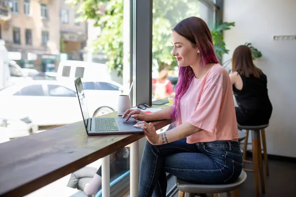 年轻的女商人坐在咖啡店餐桌旁的看法。桌杯咖啡和笔记本电脑。在背景白色墙壁和窗口. — 图库照片