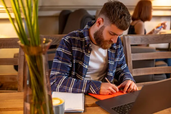 Случайный бизнесмен или фрилансер, планирующий свою работу над ноутбуком, работающий на ноутбуке со смартфоном, чашкой кофе на столе в кафе или домашнем офисе . — стоковое фото