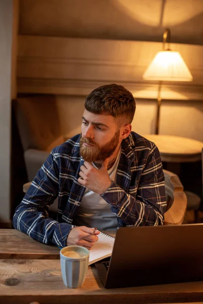 Hombre de negocios casual o freelancer planeando su trabajo en el portátil, trabajando en el ordenador portátil con teléfono inteligente, taza de café en la mesa en la cafetería o en la oficina en casa . — Foto de Stock