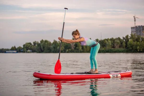 Sportieve vrouw in yoga positie op paddleboard, yoga doen op sup board, oefening voor flexibiliteit en stretching van spieren — Stockfoto