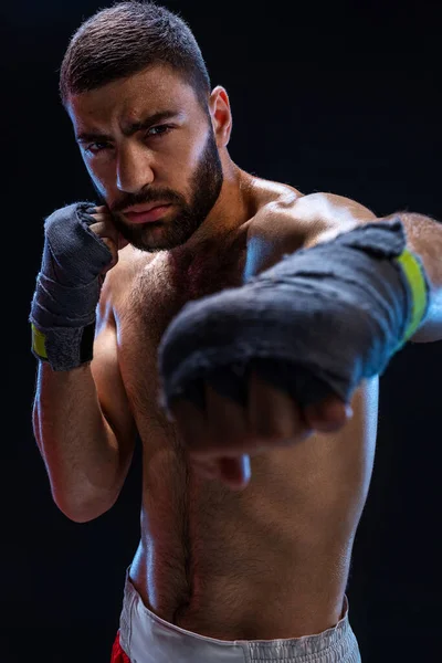 Der Boxer ist bereit, einen mächtigen Schlag zu versetzen. Foto eines muskulösen Mannes mit starken Händen und geballten Fäusten in blauen Streifen auf schwarzem Hintergrund. — Stockfoto