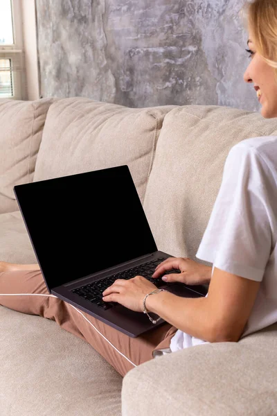 Mulher no sofá trabalhando no laptop com tela em branco mockup. Espaço de cópia vazio no monitor para propaganda. Tela preta . — Fotografia de Stock