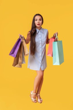 Bir alışveriş torbaları ile poz ve kameraya sarı arka plan üzerinde seyir çizgili beyaz ve mavi yazlık elbise esmer bayanın görüntüsü.