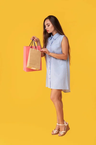 Fiatal barna hölgy, fehér és kék nyári csíkos ruha pózol a bevásárló szatyrok felső sárga háttérrel. — Stock Fotó