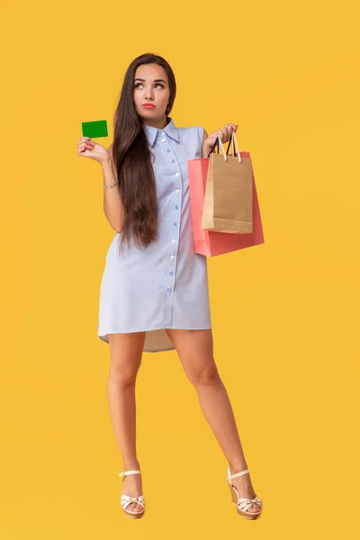 Kedves elég vonzó szexi lány mutatja a hitelkártya, és sok színes csomagok a kezében tartja, a ' kényelmesen használható bankkártyával, vásárlási, sárga háttérrel áll — Stock Fotó