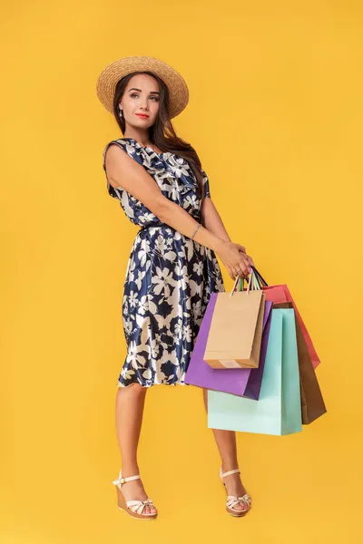 Divat portré fiatal nő visel bevásárló táskák, szalma kalap, ruha pózol át színes sárga háttér — Stock Fotó