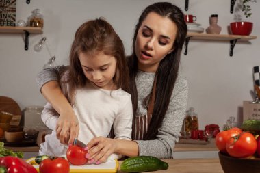 Anne ve kızı sebze salatası yapıyor ve mutfakta eğleniyor.