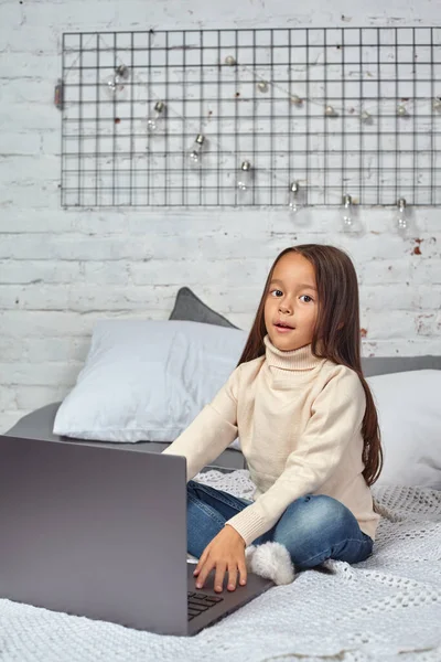 Cute little girl girl uczucie zabawne podczas oglądania kreskówek na laptopie siedzi na łóżku — Zdjęcie stockowe