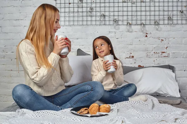 Anya és lánya teát vagy kakaót isznak az ágyon ülő nagy bögrékből. — Stock Fotó