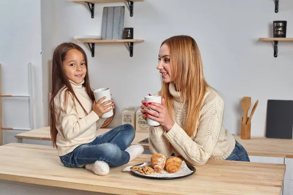 Vidám anya és lánya együtt ülnek a konyhaasztalnál, forró teát isznak reggel, kellemes baráti beszélgetést folytatnak.. — Stock Fotó