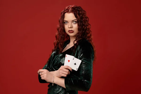 Jovem mulher sexy com um cabelo encaracolado vermelho segurando ases, em um fundo vermelho. Poker — Fotografia de Stock