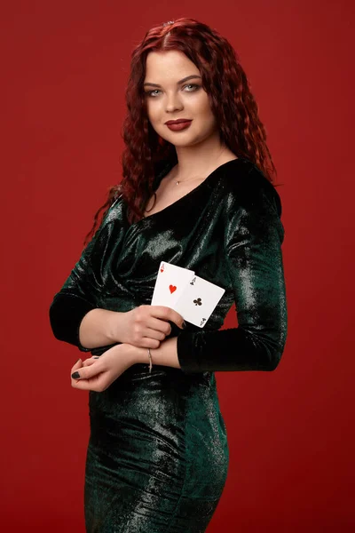 Giovane donna sexy con un rosso capelli ricci tenendo assi, su uno sfondo rosso. Poker — Foto Stock