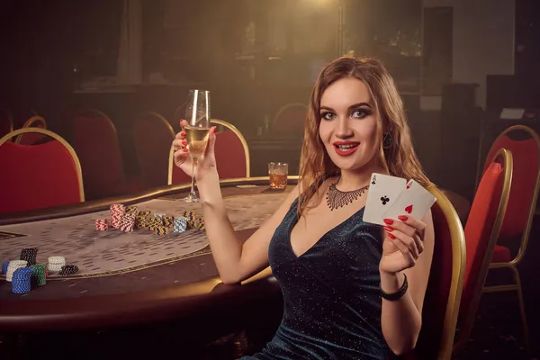 Giovane bella femmina posa seduta su una sedia contro un tavolo da poker nel casinò di lusso. — Foto Stock