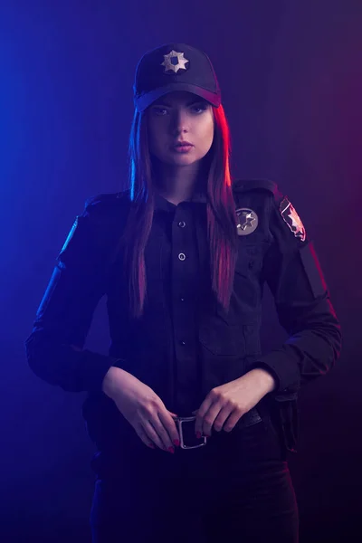 Poważne kobiece policjant jest stwarzające dla kamery na czarnym tle z czerwonym i niebieskim podświetleniem. — Zdjęcie stockowe