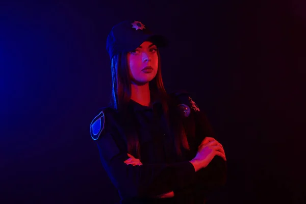 Retrato de close-up de uma policial posando para a câmera contra um fundo preto com retroiluminação vermelha e azul . — Fotografia de Stock