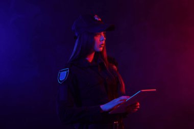 Kırmızı ve mavi arka aydınlatmalı siyah arka plan aleyhine kameraya poz veren bir kadın polis memurunun yakın çekim portresi.