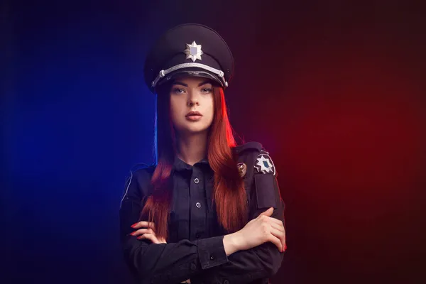 Sério policial feminino está posando para a câmera contra um fundo preto com backlighting vermelho e azul . — Fotografia de Stock