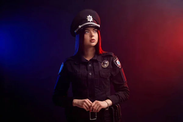 Seriöse Polizistin posiert vor schwarzem Hintergrund mit roter und blauer Hintergrundbeleuchtung für die Kamera. — Stockfoto