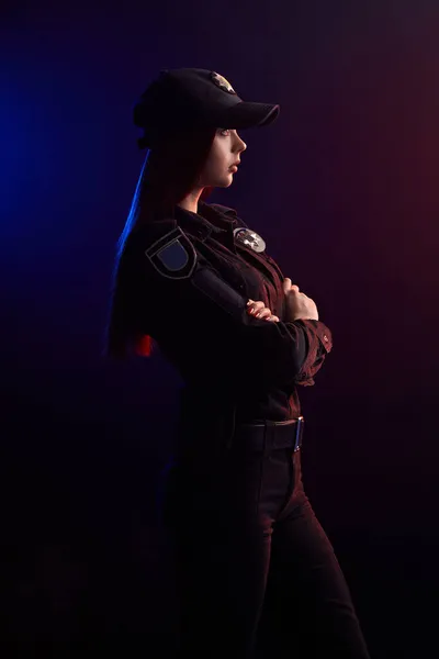 Sério policial feminino está posando para a câmera contra um fundo preto com backlighting vermelho e azul . — Fotografia de Stock