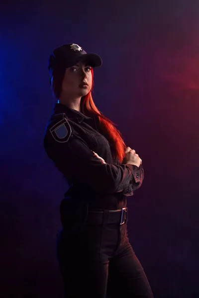 Mujer policía seria posando para la cámara sobre un fondo negro con retroiluminación roja y azul . — Foto de Stock