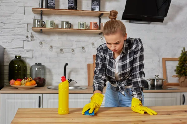 Jovem mulher em luvas de proteção limpa uma mesa na cozinha com um pano — Fotografia de Stock