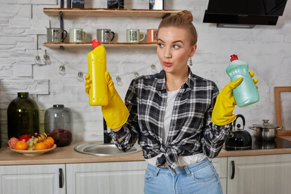 Женщина сравнивает моющие средства, она держит две бутылки и проверяет их на домашней кухне. — стоковое фото