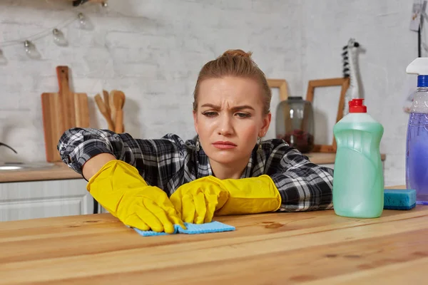 Jovem mulher em luvas de proteção limpa uma mesa na cozinha com um pano — Fotografia de Stock