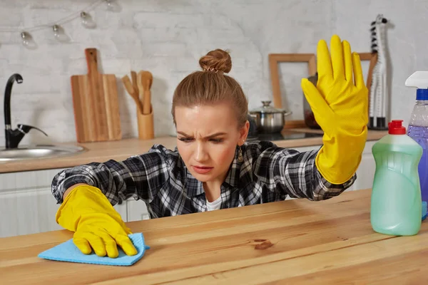 Junge Frau in Schutzhandschuhen wischt mit Lappen einen Tisch in der Küche ab — Stockfoto