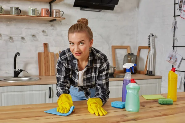 Jonge vrouw of huisvrouw in rubber handschoenen afvegen tafel met microvezel doek thuis keuken. — Stockfoto