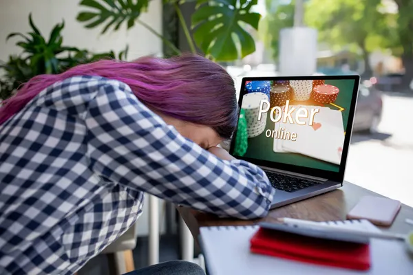 Vista lateral de una joven mujer de pelo rosa que teclea en el ordenador portátil con póquer en línea en una pantalla mientras está sentado en la cafetería. Emociones. Pérdida —  Fotos de Stock