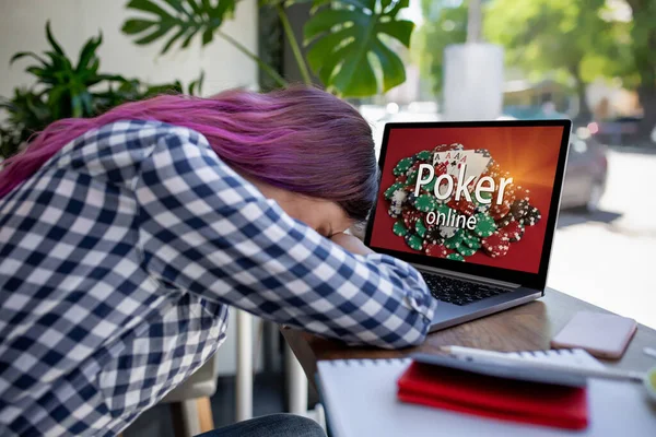 Vista lateral de una joven mujer de pelo rosa que teclea en el ordenador portátil con póquer en línea en una pantalla mientras está sentado en la cafetería. Emociones. Pérdida —  Fotos de Stock