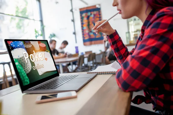Вид сбоку на молодую розововолосую женщину, сидящую в кафе на ноутбуке и играющую в покер онлайн . — стоковое фото