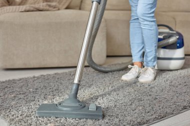 Güzel genç kadının evde halı temizlerken elektrik süpürgesi kullanarak kırpılmış görüntü