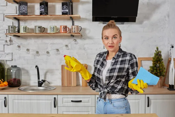 Professionale giovane donna indossa guanti di gomma protettivi gialli tenendo pulitori bottiglia in cucina. — Foto Stock