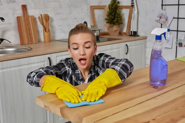 Jonge vrouw in beschermende handschoenen veegt een tafel in de keuken met een doek — Stockfoto