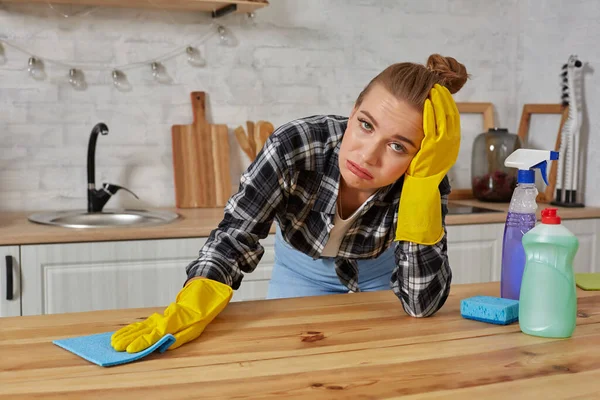 Jovem mulher em luvas de proteção limpa uma mesa na cozinha com um pano — Fotografia de Stock