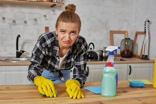 Jonge vrouw in beschermende handschoenen veegt een tafel in de keuken met een doek — Stockfoto