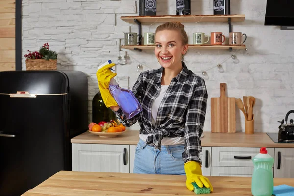 Красива жінка в захисних рукавичках прибирає кухонний стіл з ганчіркою і спреєм — стокове фото