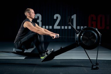 Güçlü genç adam bir t-shirt ve şort tarafına seyir spor salonunda simülatörleri egzersizleri yapıyor