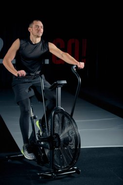Spor salonunda spor yapan erkek, kardiyo çalışması için hava bisikleti kullanıyor..