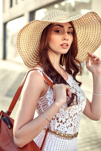 Vitrinler poz sokakta yürüyen moda esmer kadın beyaz elbiseli, hasır şapka — Stok fotoğraf
