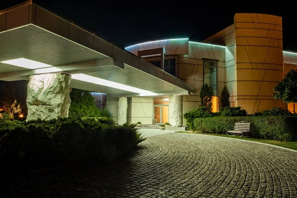 Vista nocturna de la entrada principal del hotel con porche en columnas rocosas y camino de acceso pavimentado — Foto de Stock
