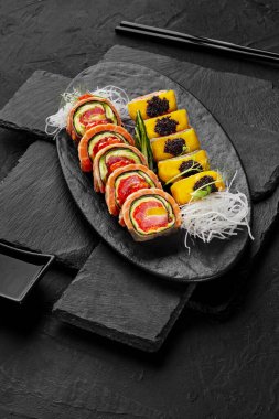 Suşi, ton balığı, somon, mango kırmızı havyar ve siyah arka planda tobiko ile süslenmiş avokado.