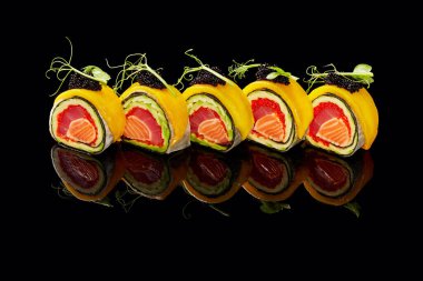 Pirinçsiz suşi rulosu ton balığı, somon, tobiko, avokado üzeri mango, siyah arka planda havyar.