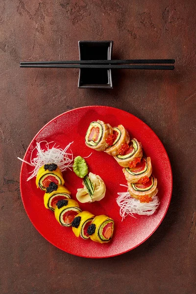 Rolls with tuna, salmon, mango, avocado, caviar served on red plate on textured brown countertop — 图库照片