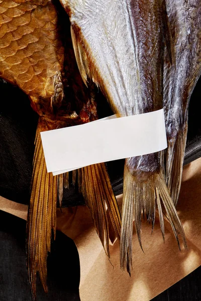 Хвосты на копченой и сушеной соленой рыбе с этикеткой на черном фоне с крафтовой бумагой — стоковое фото