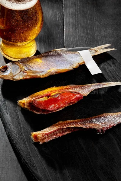 Whole and skinned salted sun-dried roach with roe served with pale lager on black background