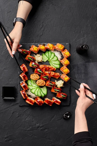 Two female hands using chopsticks to take rolls from sushi set — 图库照片