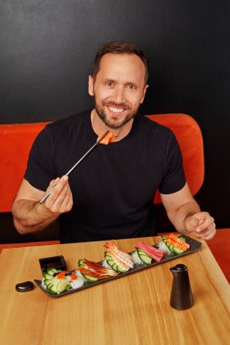 Positive man eating delicious Japanese assorted sashimi set in cafe clipart